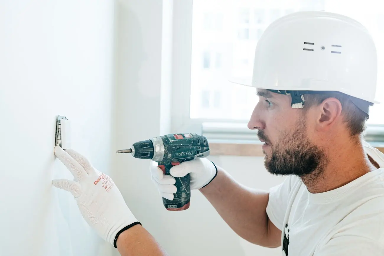 Profissional de capacete instalando acabamento em parede durante reforma