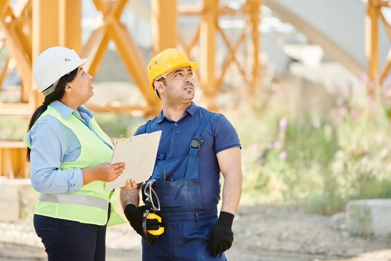Técnica de segurança com prancheta orientando um trabalhador no canteiro de obras
